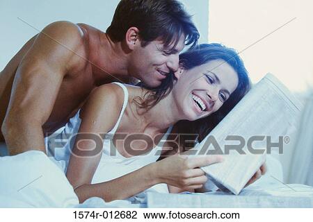 Stock Image - Young couple reading a newspaper in bed. Fotosearch