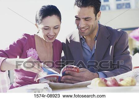 Stock Image - Young couple sitting in a restaurant reading a book. Fotosearch