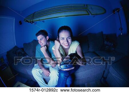 Young couple sitting on a couch watching a television View Large Photo Image Stock Image - Young couple sitting on a couch watching a television. Fotosearch