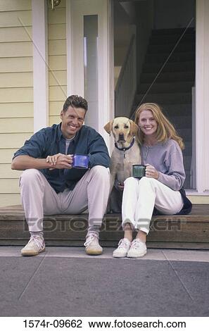 Stock Image - Young couple sitting on the front porch with their dog. Fotosearch