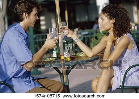 Stock Photography - Young couple sitting outdoors toasting. Fotosearch
