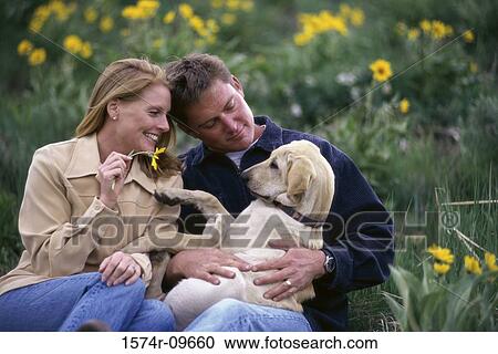 Stock Image - Young couple sitting together with a dog in a park. Fotosearch