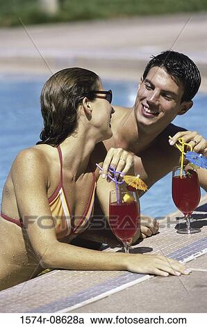 Stock Image - Young couple together in a swimming pool with drinks. Fotosearch