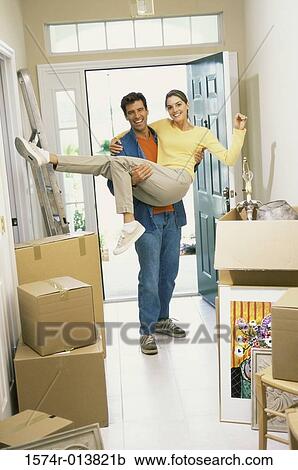 Stock Image - Young man carrying a young woman over the threshold of their new home. Fotosearch