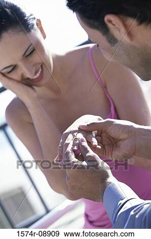 Young man putting an engagement ring on a young woman's finger View Large Photo Image Stock Photo - Young man putting an engagement ring on a young woman's finger. Fotosearch