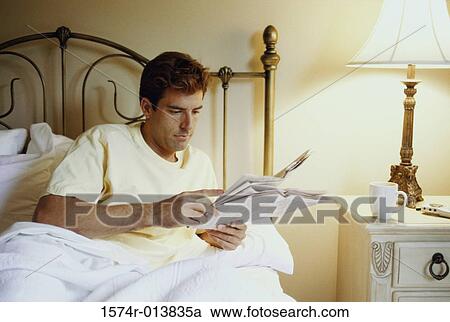 Young man reading a newspaper in bed View Large Photo Image Stock Image - Young man reading a newspaper in bed. Fotosearch