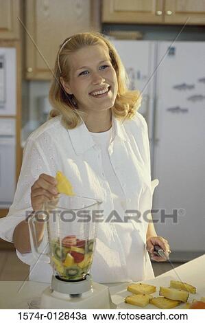 Stock Image - Young pregnant woman putting fruit in a blender. Fotosearch