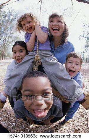 Stock Image - Young woman and four children playing on a tire swing. Fotosearch