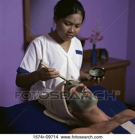 Picture - Young woman applying a facial mask. Fotosearch