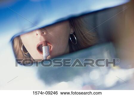 Young woman applying lipstick in the rear view mirror of a car View Large Photo Image Stock Photograph - Young woman applying lipstick in the rear view mirror of a car. Fotosearch