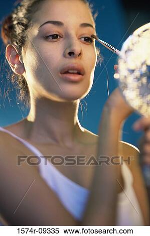 Young woman applying make-up in front of a mirror View Large Photo Image Stock Photography - Young woman applying make-up in front of a mirror. Fotosearch