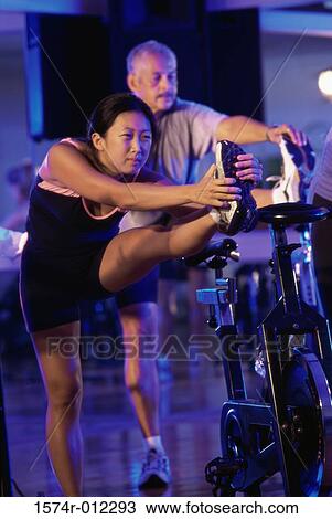 Stock Image - Young woman exercising with a mature man in a gym. Fotosearch