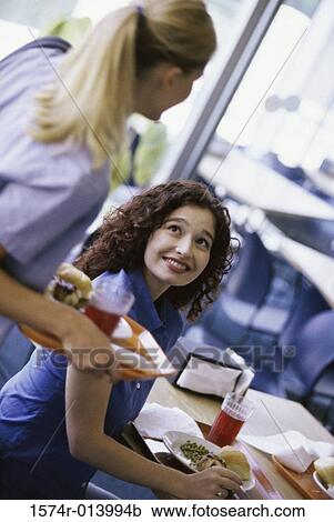 Young woman holding a tray of food looking at a woman seated at a table View Large Photo Image Stock Image - Young woman holding a tray of food looking at a woman seated at a table. Fotosearch