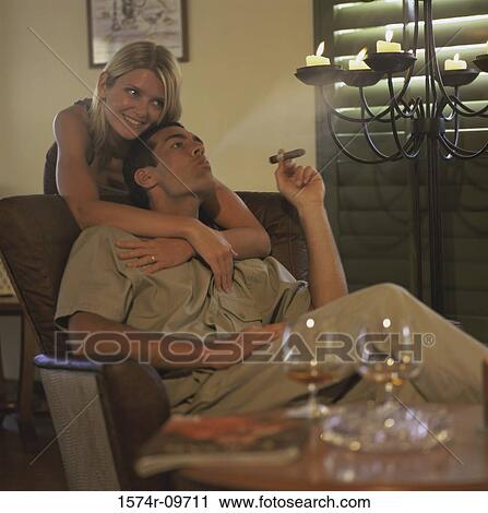 Stock Image - Young woman holding a young man smoking a cigar. Fotosearch