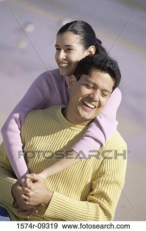 Stock Photo - Young woman riding piggyback on a young man at the beach. Fotosearch