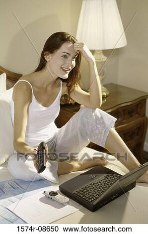 Young woman sitting on a bed in front of a laptop View Large Photo Image Stock Image - Young woman sitting on a bed in front of a laptop. Fotosearch