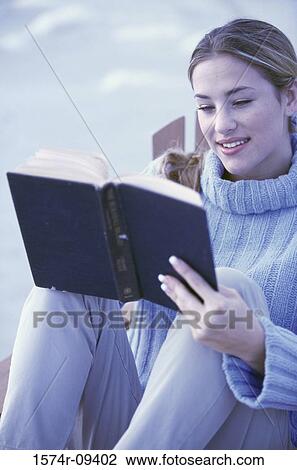 Young woman sitting outdoors reading a book View Large Photo Image Stock Image - Young woman sitting outdoors reading a book. Fotosearch
