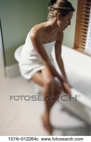 Stock Image - Young woman wrapped in a towel sitting on the edge of a bathtub. Fotosearch