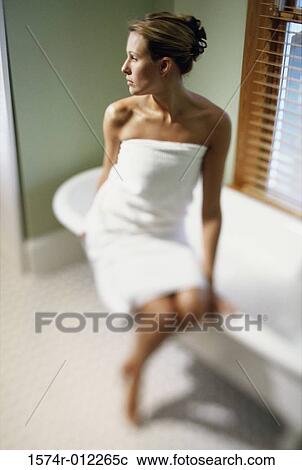Stock Image - Young woman wrapped in a towel sitting on the edge of a bathtub. Fotosearch