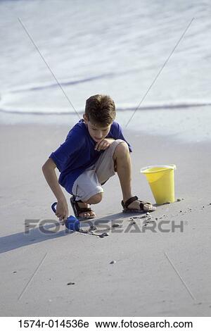 Boy digging sand with a shovel on the beach View Large Photo Image Stock Image - Boy digging sand with a shovel on the beach. Fotosearch