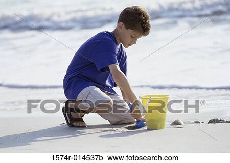 Stock Image - Boy digging sand with a shovel on the beach. Fotosearch