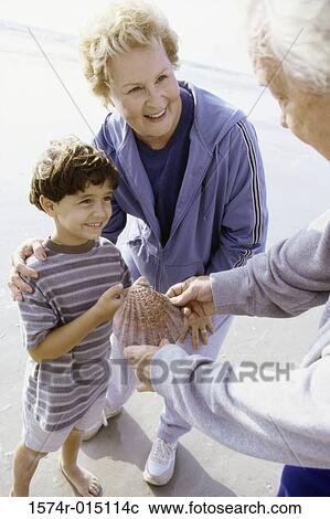 Stock Image - Boy holding a seashell on the beach with his grandparents. Fotosearch