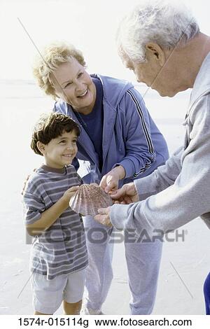 Boy holding a seashell on the beach with his grandparents View Large Photo Image Stock Image - Boy holding a seashell on the beach with his grandparents. Fotosearch