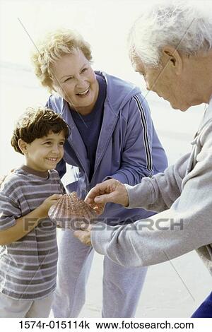 Stock Image - Boy holding a seashell on the beach with his grandparents. Fotosearch