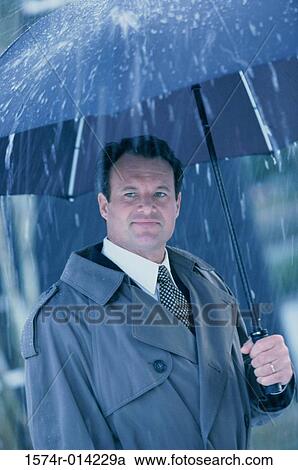 Stock Image - Businessman holding an umbrella in the rain. Fotosearch