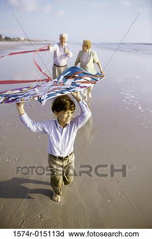 Stock Image - Child flying a kite on the beach with his grandparents. Fotosearch