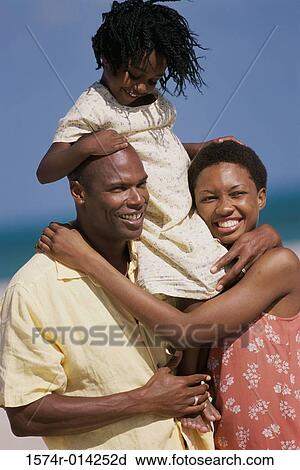 Stock Image - Close-up of a daughter riding on her father's shoulders on the beach with her mother standing beside them. Fotosearch