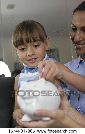Stock Photography - Close-up of a daughter with her mother inserting a coin into a piggy bank. Fotosearch