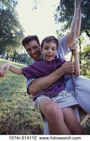 Stock Image - Close-up of a father and son swinging on a rope swing. Fotosearch