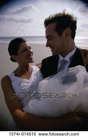 Stock Photography - Close-up of a groom carrying his bride on the beach. Fotosearch