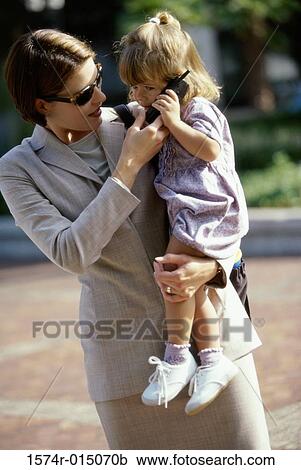 Stock Image - Close-up of a mother carrying her daughter talking on a mobile phone. Fotosearch