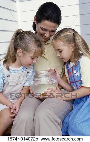 Close-up of a mother sitting with her two daughters looking at a fishbowl View Large Photo Image Stock Image - Close-up of a mother sitting with her two daughters looking at a fishbowl. Fotosearch