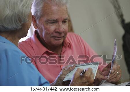 Close-up of a senior woman signing a check with a senior man sitting beside her View Large Photo Image Stock Image - Close-up of a senior woman signing a check with a senior man sitting beside her. Fotosearch