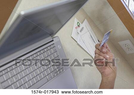 Stock Image - Close-up of a woman's hand holding a credit card in front of a laptop. Fotosearch
