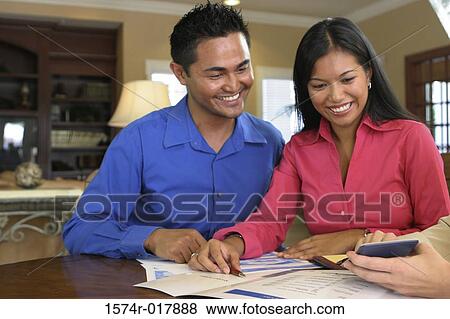Close-up of a young couple looking at a calculator smiling View Large Photo Image Stock Photo - Close-up of a young couple looking at a calculator smiling. Fotosearch