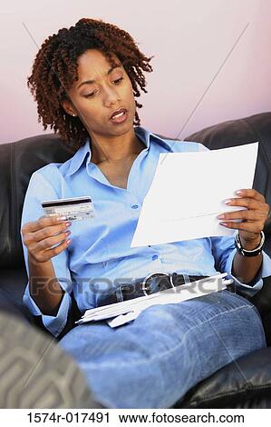 Stock Image - Close-up of a young woman holding a credit card reading a bill. Fotosearch