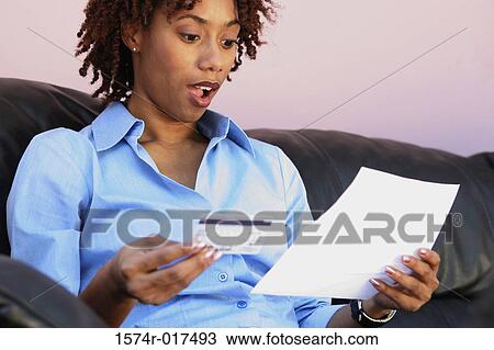 Stock Image - Close-up of a young woman holding a credit card reading a bill. Fotosearch