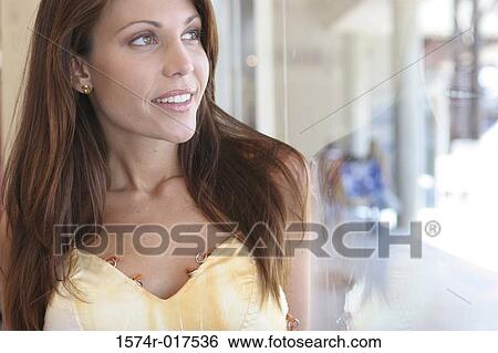 Stock Photograph - Close-up of a young woman looking through a window. Fotosearch