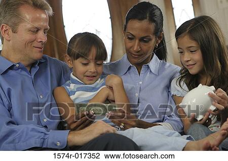 Stock Image - Close-up of parents sitting with their two daughters looking at money. Fotosearch
