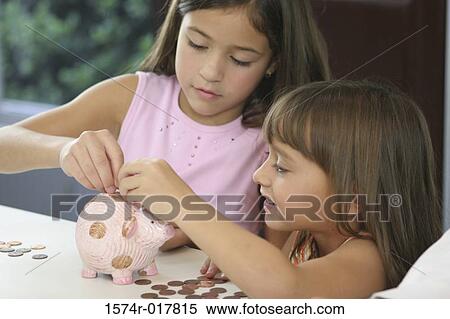 Stock Photography - Close-up of two sisters inserting coins into a piggy bank. Fotosearch