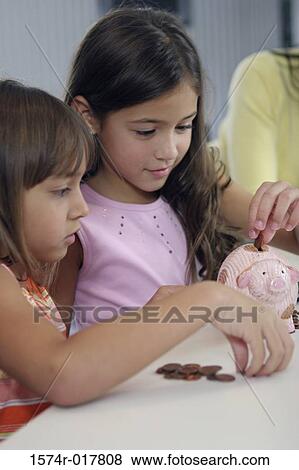Close-up of two sisters looking at a piggy bank with their mother standing behind them View Large Photo Image Stock Photo - Close-up of two sisters looking at a piggy bank with their mother standing behind them. Fotosearch