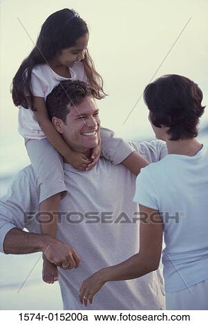 Daughter on her father's shoulders at the beach with her mother standing in front of them View Large Photo Image Stock Image - Daughter on her father's shoulders at the beach with her mother standing in front of them. Fotosearch