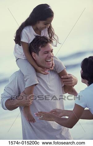 Daughter on her father's shoulders at the beach with her mother standing in front of them View Large Photo Image Stock Image - Daughter on her father's shoulders at the beach with her mother standing in front of them. Fotosearch