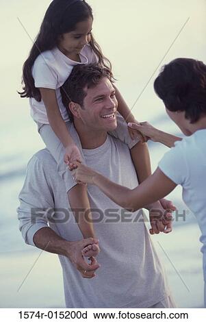 Daughter on her father's shoulders at the beach with her mother standing in front of them View Large Photo Image Stock Image - Daughter on her father's shoulders at the beach with her mother standing in front of them. Fotosearch
