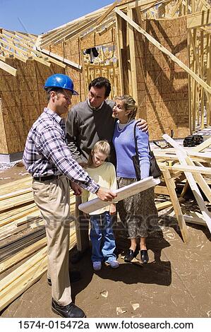 Stock Image - Family standing at a construction site with a worker holding blueprints. Fotosearch