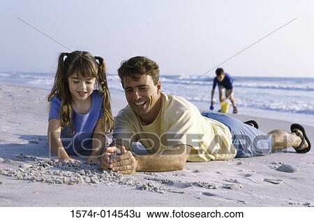 Stock Photograph - Father and his daughter making a sand castle on the beach. Fotosearch